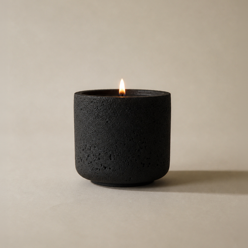 the andromeda candle lit, black hand-cast concrete vessel on a cream ground